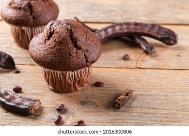 Chocolate carob cupcakes cooking with carob powder and dried carob pods on a wooden background. Organic healthy sweet food for vegan vegetarian food and drinks, close up