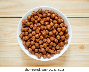 Chocolate cereal balls in a bowl on wooden background. Healthy breakfast concept. Top view.
