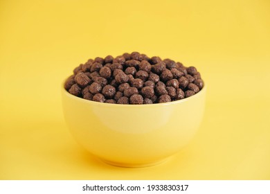 Chocolate cereal corn balls in a yellow bowl on a yellow background. Copy, empty space for text.