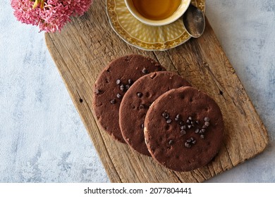 Chocolate chip cookies with a cup of black tea on a wooden cutting board on a white tablecloth with pink flowers