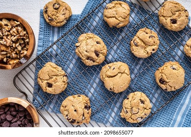 Chocolate Chip Cookies On A Cooling Rack On Top Of A Blue Dish Towel With Bowels Of Chocolate Chips And Walnuts