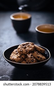 Chocolate chip cookies on a dark background with tea and teapot in background