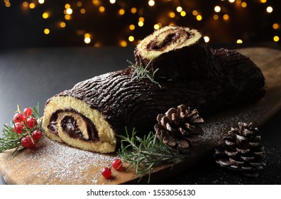 Chocolate Christmas Yule Log, Buche de Noel on wooden cutting board. Christmas decoration on dark background. Closeup