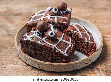 Chocolate cobweb brownies with candy spiders, homemade treats for Halloween on rustic wooden background