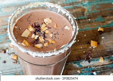 Chocolate coconut smoothie milkshake blended with cacau, coconut milk, banana and topped with coconut flakes and chia seeds. A healthy snack or treat served in a tall glass on a rustic wooden table.
