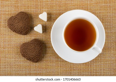 Chocolate Cookies In Form Heart, Two Pieces Of Sugar, Cup Of Tea On Saucer On Brown Mat. Top View