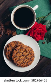 Chocolate cookies on a plate, red rose on a green napkin, coffee beans, coffee mug.