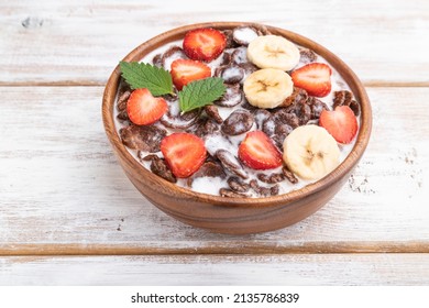 Chocolate cornflakes with milk and strawberry in wooden bowl on white wooden background. Side view, close up.