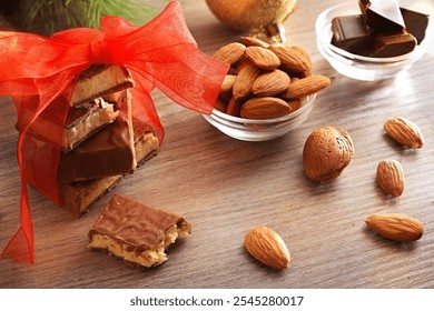 Chocolate covered nougat with stacked pieces tied with red ribbon on a wooden bench with natural almonds and portions of chocolates and festive decoration. Top elevated view. - Powered by Shutterstock