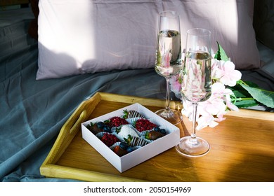 Chocolate covered strawberries, two glasses of champagne and flowers are on a tray on the bed. The concept of newlyweds and February 14