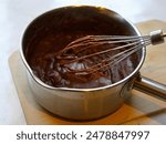 Chocolate cream for pie, dessert, sweets and cake in a saucepan with a whipping pattern on a wooden board on a white background. Pastry shop and pastry chef, cooking, kitchen worker, kitchen