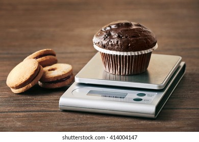 Chocolate cupcake and digital kitchen scales on wooden table