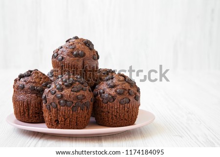 Chocolate cupcakes on pink plate on white wooden surface, side view. Close-up. Copy space.