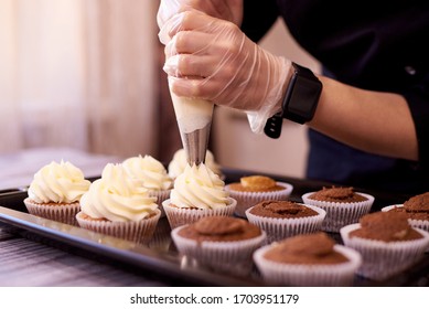 Pasteles de chocolate con un poco de crema. Las manos femeninas llenan los pasteles en una hoja de hornear.