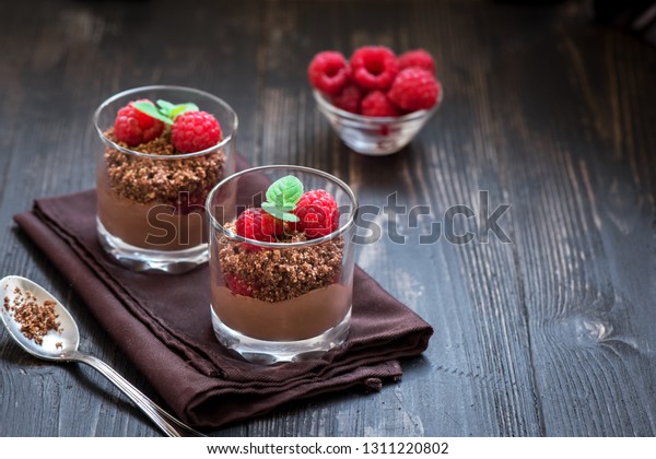 Chocolate\
dessert in glasses with raspberries. Chocolate mousse or pudding in\
portion glasses with fresh berries, copy\
space.