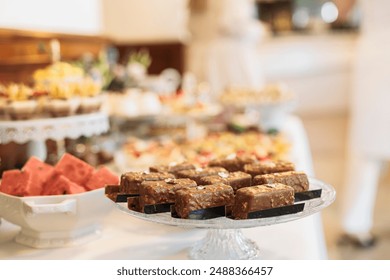 Chocolate desserts and watermelon on white tablecloth, with silver platter and black accents. Blurred indoor setting with person in background - Powered by Shutterstock