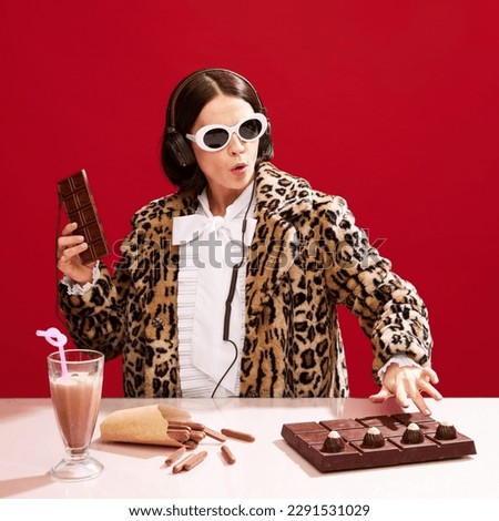 Chocolate dj station. Woman in stylish sunglasses and animal print coat playing music set with chocolate equipment over red background. Concept of pop art, creativity, food, inspiration