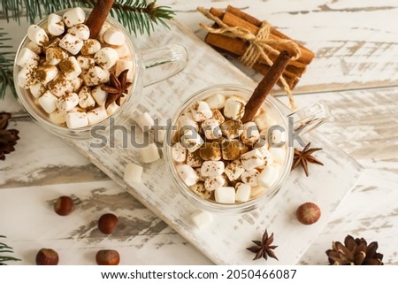 chocolate drink or cocoa with marshmallow in glass mugs on a white wooden table. top view of the drink cinnamon sticks, nuts, anise stars