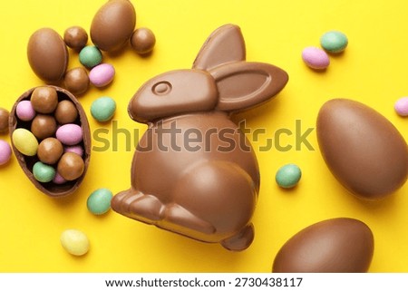 Chocolate Easter bunny and eggs on yellow background, flat lay