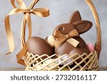 Chocolate Easter bunny and eggs in wicker basket against light grey background, closeup
