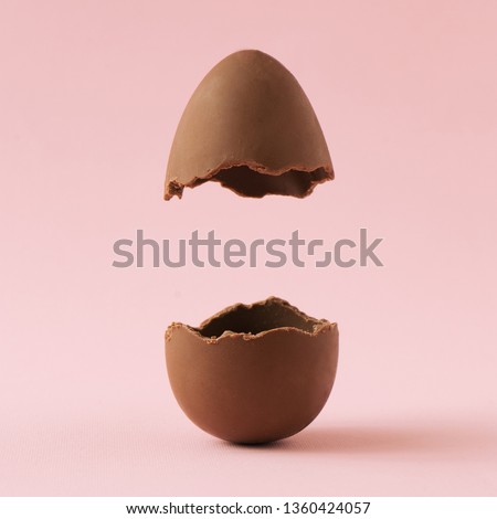 Chocolate Easter egg broken in half on pastel pink background with creative copy space. Minimal Easter holiday concept.