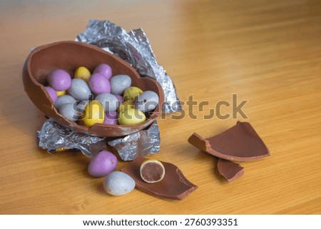 Chocolate Easter egg broken open with colorful candy eggs on woo