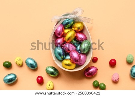 Chocolate Easter eggs in foil with bow and candies on beige background