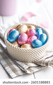 Chocolate easter eggs wrapped in multi colored foil in bowl on a white table.
