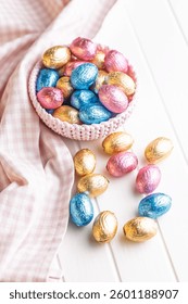 Chocolate easter eggs wrapped in multi colored foil in bowl on a white table.