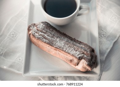 Chocolate eclair on the plate and cup of black coffee