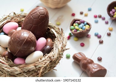 Chocolate eggs and easter almonds on bird nest, chocolate bunny and sweets on white wooden table