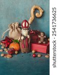 Chocolate figurine of St. Nicholas with gifts against a blue wall. Holiday background Saint Nicholas, Sinterklaas, gifts for children with cookies, chocolate, nut, tangerines and sweets