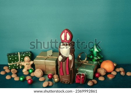 Chocolate figurine of St. Nicholas with gifts against a blue wall. Holiday background Saint Nicholas, Sinterklaas, gifts for children with cookies, chocolate, nut, tangerines and sweets
