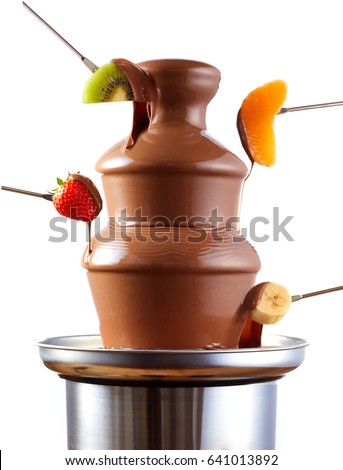 Chocolate fondue fountain with fresh tropical fruit on forks being dipped in the rich creamy sauce in a side view isolated over white