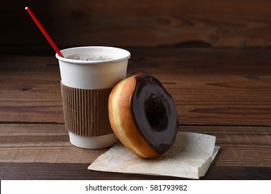 A Chocolate Frosted Donut Or Doughnut Leaning On A Hot Cup Of Fresh Brewed Coffee. 