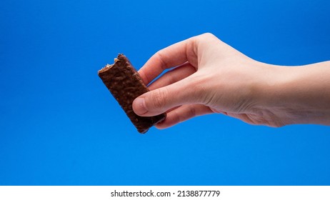 Chocolate Granola Bar With Bite Taken In Hand On A Blue Background