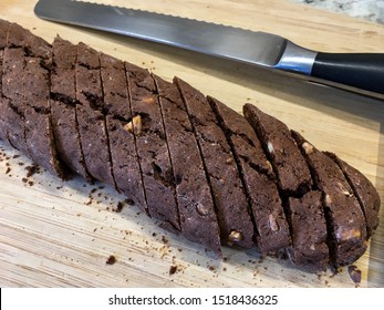 Chocolate hazelnut biscotti cookie log, sliced with a serrated knife, on a wooden board. 