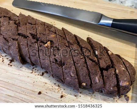 Chocolate hazelnut biscotti cookie log, sliced with a serrated knife, on a wooden board. 