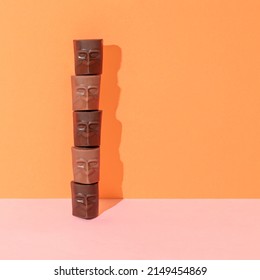 Chocolate heads tower with sunshine shadow against bright pink and orange background. Minimal candy food concept. Creative dessert composition.