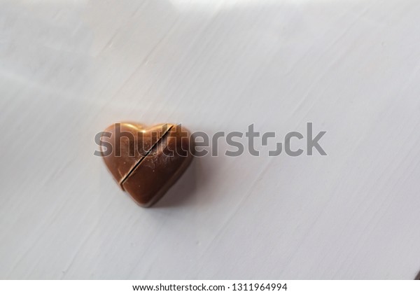 Chocolate heart candy cut in half on white wooden\
table with copy space