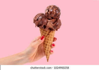 Chocolate ice cream cone on pink faded pastel color background. Hand holding chocolate ice cream in wafer cup.