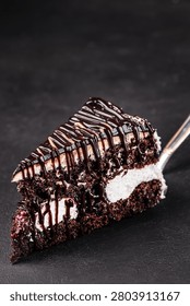 Chocolate layer cake slice with whipped cream, berry filling and chocolate drizzle on fork over dark background. Premium dessert concept.