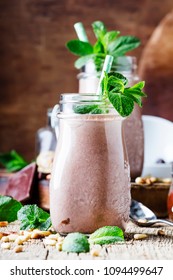 Chocolate milkshake or cocktail with nuts and mint leaves, old wooden background, selective focus