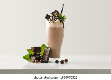 Chocolate milkshake with cream decorated chocolate portions and balls around on white wooden table and light isolated background. Front view.