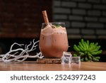 chocolate milkshake topped with ice cream, mint leaves, sprinkled with nuts, wafer roll, which is on a wooden base and added with ice props and also white wooden twigs