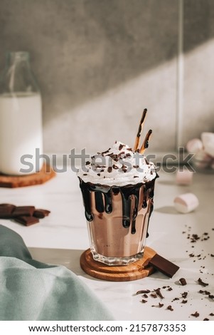 Chocolate milkshake with whipped cream served in glass on the light gray table.