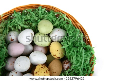 Chocolate mini Easter eggs in green straw on a whicker basket against a white background
