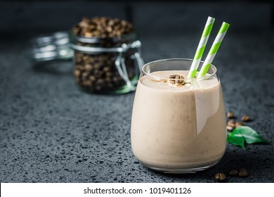 Chocolate mocha breakfast smoothie and coffee beans in glass jar on dark concrete background. Selective focus, space for text. 