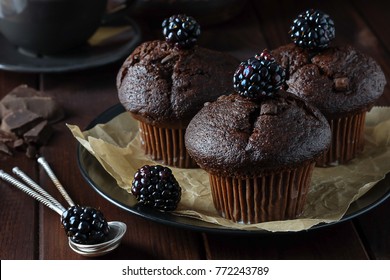 Chocolate muffins decorated with blackberry on dark-brown background. Closeup. Photo in dark-key.