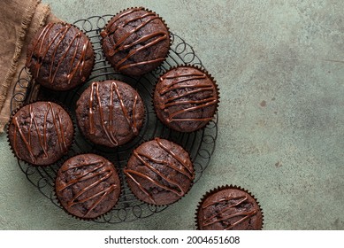 Chocolate muffins decorated with melted chocolate top view. Homemade cakes on black metal cooling rack, brown textile. Dark green background. Delicious sweet cupcakes. Copy space. - Powered by Shutterstock